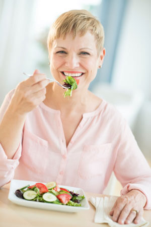 Woman with short blonde hair eating a plate of vegetables.