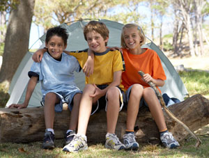 Three young kids sitting on a log in front of a tent.