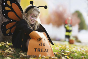 Young blonde girl wearing a butterfly costume looking in her Trick or Treat bag.