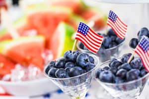 Three small bowls of blueberries with American flags in them and a bowl of watermelon in the background.