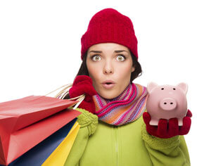 Woman wearing a red beanie and scarf holding bags in one hand and a piggy bank in the other.