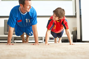 Man and boy doing a plank in a room, both wearing jerseys.