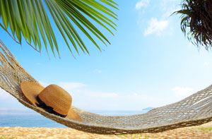Beach scene with a hammock with a hat set on it.