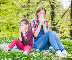 Young girl and woman sitting on grass blowing their nose.