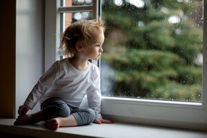 Young child sitting on a nook looking out the window.