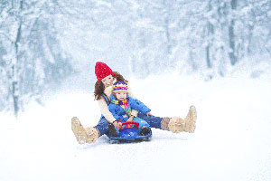 Young child and woman sledding in the snow.