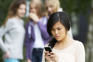 Teenage girl looking at her phone with a group of girls in the background looking at her.
