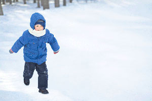 Young child in blue snow jacket running in the snow.