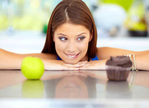Woman looking at an apple and a cupcake.