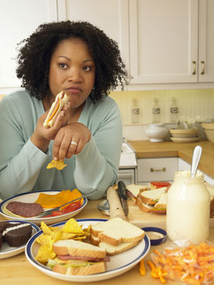 Woman eating a sandwich in a kitchen.