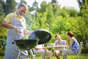 Male in an apron barbecuing with people sitting in the background