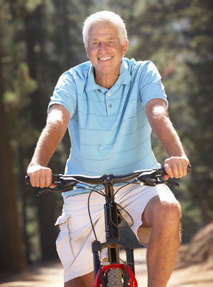 Older man in a light blue polo on a bike outside.