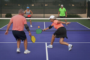 Four people playing paddle ball on a blue tennis court.