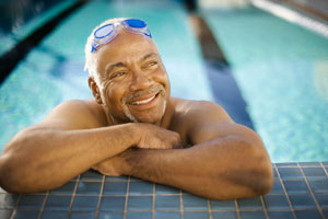 Older man in a swimming pool with goggles on his head.