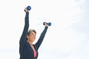 Older woman holding two small dumbbells outside.