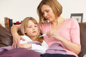 Woman with short hair sitting on the couch with young girl looking at a thermometer.