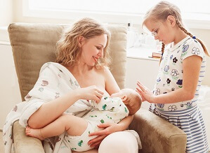 woman breastfeeding baby with little girl standing next to her