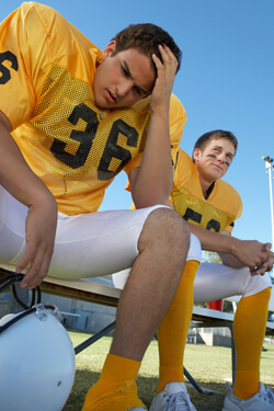 Two football players wearing yellow jerseys sitting on a bench.