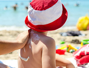 person putting sunscreen on child's back at the beach