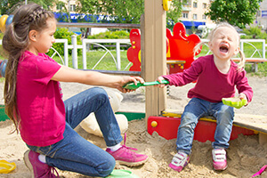 Two young girls pulling on a green shovel, the younger of the two is crying.